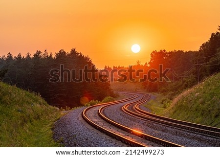 The setting sun against the background of the international railway line passing through the forest. Sunset lighting. Winding road. Railway infrastructure. Royalty-Free Stock Photo #2142499273