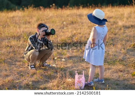 A teenage boy takes pictures of his younger sister with a camera in nature in the soft light of the setting sun. Copy space. Selective focus.                               
