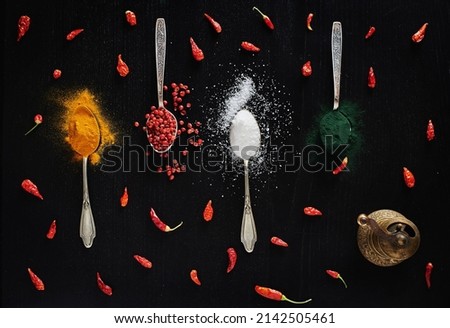 Various types of spices displayed on black background in tea spoons. Top view over turmeric, red pepper, chilli pepper,salt and spirulina powder colorful arrangement Royalty-Free Stock Photo #2142505461