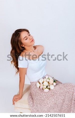 Happy young woman with close eyes and long curly hair in a white dress with a bouquet of flowers isolated on a white background. Beautiful girl with flowers. Copy space.