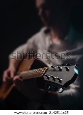 The guitarist is playing acoustic guitar shown in small depth of field where the focus is on the headstock. Dark and moody. Royalty-Free Stock Photo #2142511635