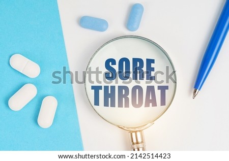 Medical concept. On a white and blue surface are pills, a pen and a magnifying glass with the inscription - SORE THROAT