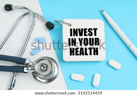 Medical concept. On a white and blue surface are pills, a stethoscope, a pen and a notepad with the inscription - INVEST IN YOUR HEALTH