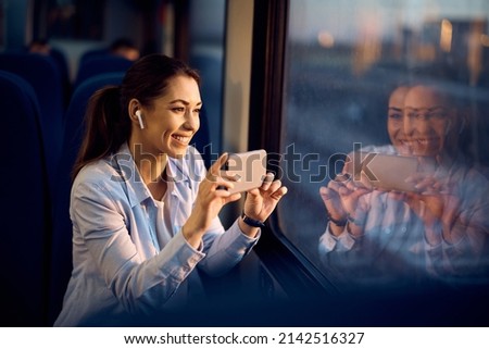 Happy tourist using her smart phone and taking picture through the window while traveling by train.