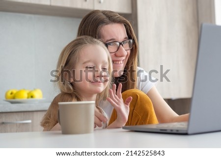 Mother with daughter sitting on the modern kitchen and watching a learning video on a laptop. Home Education concept