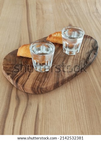 Two glasses with a strong colorless alcoholic beverage and dough patties on an old wooden tray. Ice vodka with snack. Buffet, aperitif