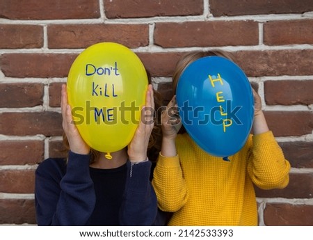 two unrecognizable people with blue yellow balloons instead of face with inscriptions dont kill me and help. Children against war. Fear, despair, drawing attention to military conflict in Ukraine
