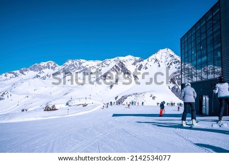 Skiers waiting at ski station. Snow covered mountains against blue sky. Tourists enjoying adventure sport in alps.