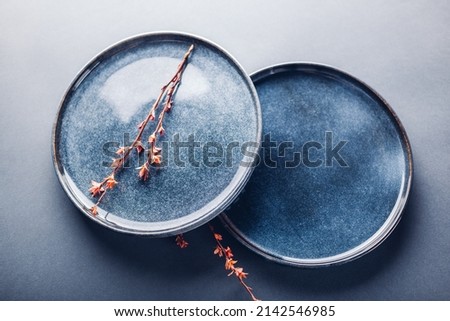 Handmade ceramic plates decorated with spring branches. Close up of lacquered blue vintage dishes on grey background. Stylish modern pottery. Space