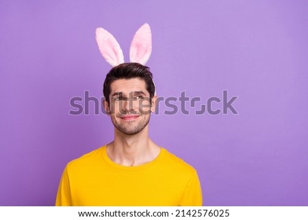 Photo of cute good mood young man with funny bunny ears look empty space daydreaming isolated on violet color background