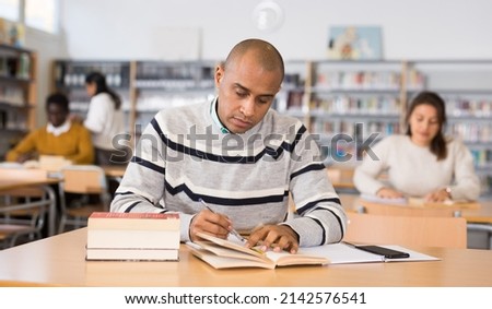 Portrait of focused adult latin american student studying in university library, making notes Royalty-Free Stock Photo #2142576541
