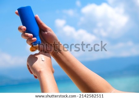 A woman is applying sunscreen and skin care to protect her skin from UV rays. She is applying sunscreen on her hand and arm. The sun symbol is a very sunny background. Health and skin care concept Royalty-Free Stock Photo #2142582511