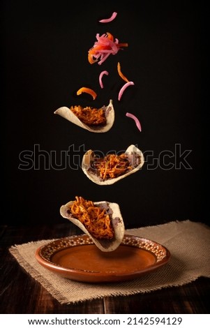 Creative food image of Mexican Tacos de Cochinita Pibil and onion with habanero chili falling on traditional mexican clay dish. Levitation photography. Royalty-Free Stock Photo #2142594129