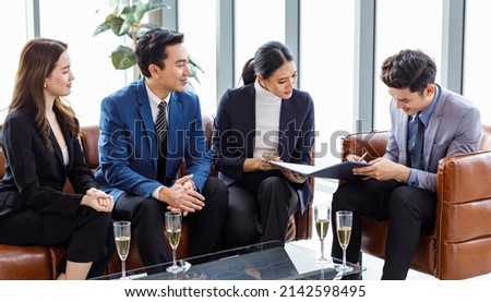 Asian professional successful male businessman customer in formal business suit sitting on leather sofa signing signature on contract agreement while happy company sales staffs smiling when job done.