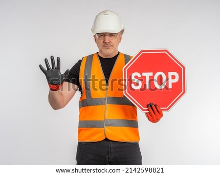Builder warns danger. Stop sign in hand of builder. Builder demands to stop. Man in work uniform shows stop gesture. Preventing dangerous situation. Danger on road concept. Worker on light background