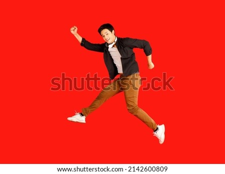 Smile Asian handsome male model wearing headphones and jumping pose for photographing by happy mood isolated on red background.