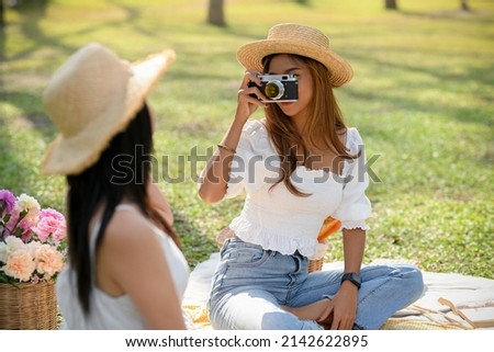 Two female best friends enjoying picnic in the green park together, Female taking a picture of her friends with retro camera.