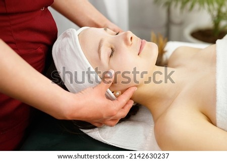 Close up photo of a amazing young woman face with closed eyes undergoing face massage procedure in spa salon, face care concept.