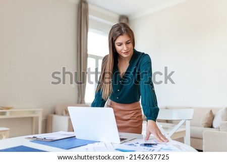Smiling young female employee stand at desk in office look in distance thinking or visualizing career success. Happy businesswoman plan or dream at workplace. Business vision concept.
