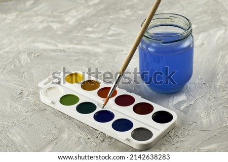 watercolor paints a paint brush and a jar of water on a gray surface. High quality photo