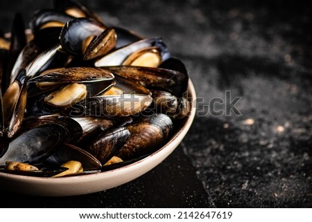 Full bowl with boiled mussels on a stone board. On a black background. High quality photo
