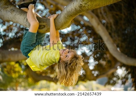 Happy kids climbing up tree and having fun in summer park. Kids climbing trees, hanging upside down on a tree in a park. Child protection. Childhood concept. Royalty-Free Stock Photo #2142657439