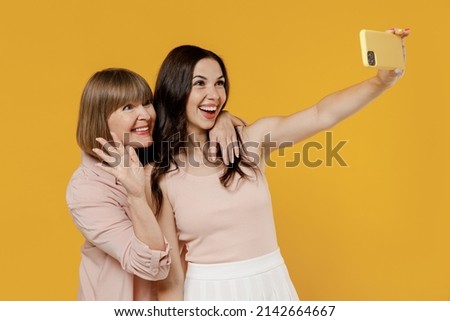 Two side view young happy daughter mother together couple women in casual clothes do selfie shot mobile cell phone post photo on social network waving hand isolated on plain yellow background studio