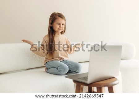 addicted to modern technology, joyful little cute girl sitting on the couch with a computer, enjoying entertaining online games, socializing on social networks, watching funny video content