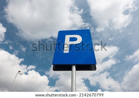 Parking sign indicator in a parking lot photographed against blue sky with white clouds. Transportation industry.