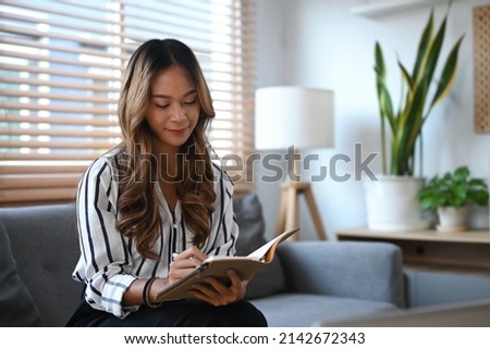 Photo of attractive woman in casual clothes relaxing on couch and reading a book in living room.