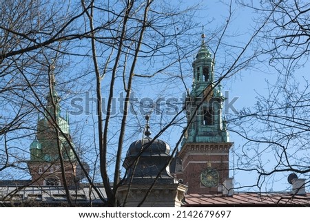 Spiers on two towers of Wawel Castle in Krakow behind tree branches against a blue sky
