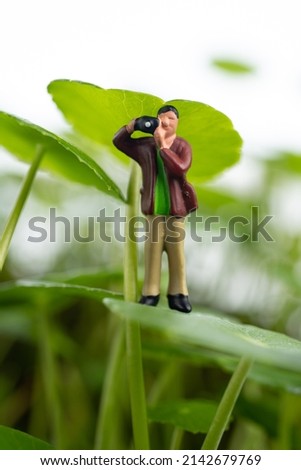 miniature photographer holding a camera in green world. Outdoors photograph concept.