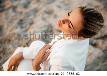 Charming fashion model with closed eyes having professional photo session in sand quarry. Young woman with blond hair enjoying favorite hobby on fresh air.