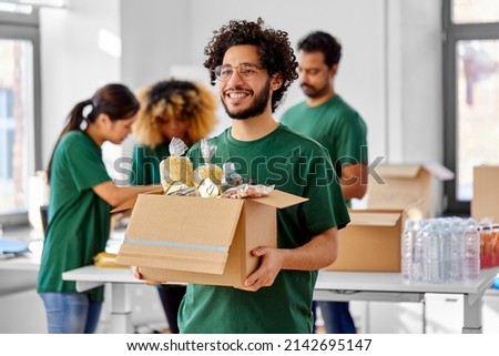 charity, donation and volunteering concept - happy smiling male volunteer with food in box and international group of people at distribution or refugee assistance center Royalty-Free Stock Photo #2142695147