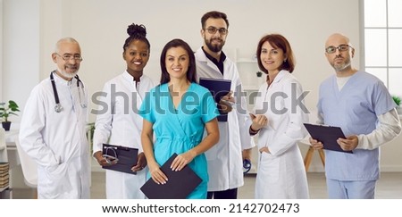 Multiethnic staff in clinic or hospital. Diverse team of happy doctors, general practitioners, specialists and nurses in scrubs and white lab coat uniforms standing in office and smiling at camera Royalty-Free Stock Photo #2142702473