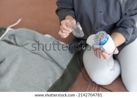 Wireless device for cleaning knitted fabrics from lint. The woman is removing the lint from the sweater. Royalty-Free Stock Photo #2142704781