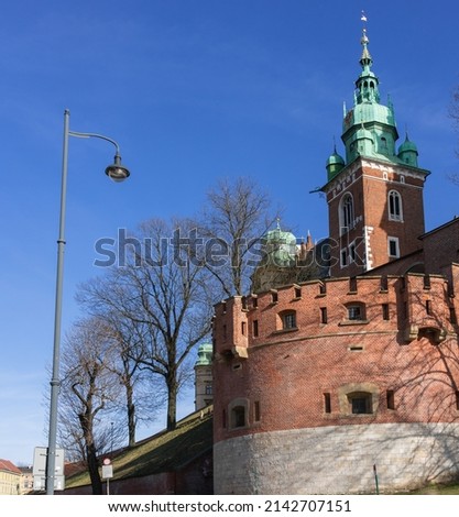 Red brick wall and tower at the entrance to the Wawel Royal Castle in Krakow, spring trees under the blue sky against the blue sky on a sunny day