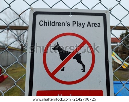 A sign attached to a chain link fence that says "CHILDREN'S PLAY AREA". There is a symbol or pictogram showing that no animals, pets, or dogs are allowed.