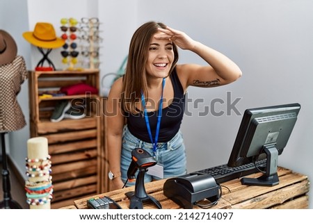 Young brunette woman holding banner with open text at retail shop very happy and smiling looking far away with hand over head. searching concept. 