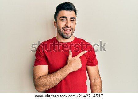 Young hispanic man wearing casual clothes smiling cheerful pointing with hand and finger up to the side 