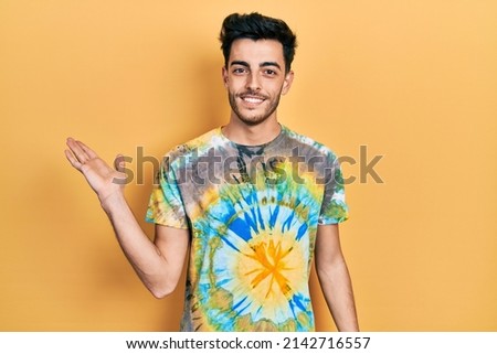Young hispanic man wearing casual clothes smiling cheerful presenting and pointing with palm of hand looking at the camera. 