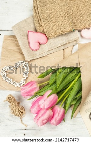Bouquet of fresh pink tulips. Making spring floral decorations. Tools, vintage scissors, craft paper, soft hearts. White wooden boards background, top view