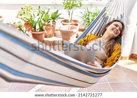 Young hispanic girl using laptop lying on hammock at the terrace. Royalty-Free Stock Photo #2142721277