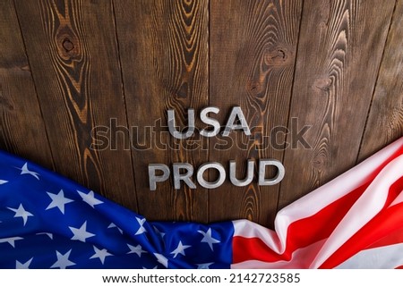 words USA proud laid with silver metal letters on brown wooden surface with flag of United States of America in linear perspective.