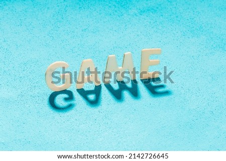 game - a word laid out of wooden letters on a blue canvas. the letters cast a shadow on the canvas. word shadow