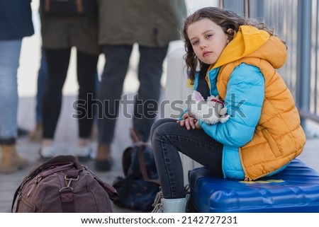 Sad Ukrainian immigrant child with luggage waiting at train station, Ukrainian war concept. Royalty-Free Stock Photo #2142727231