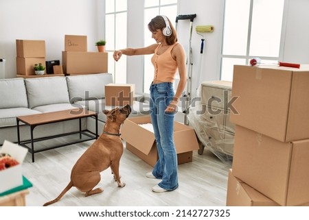 Young caucasian woman listening to music feeding dog at home