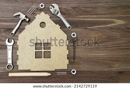 Set of miniature hand tools and fasteners arranged around a flat house model on a wooden background with copy space. Royalty-Free Stock Photo #2142729119