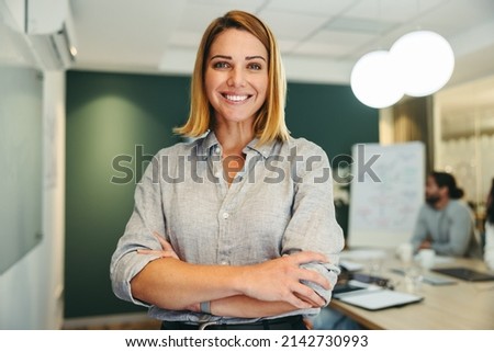Successful female manager smiling at the camera while standing in a boardroom. Cheerful businesswoman attending a meeting with her colleagues in a modern workplace. Royalty-Free Stock Photo #2142730993