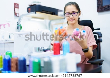 Embroidery, handicrafts, SME, family business Portrait of an Asian female designer picking up sewing threads for Design patterns using automatic embroidery machines according to customer orders